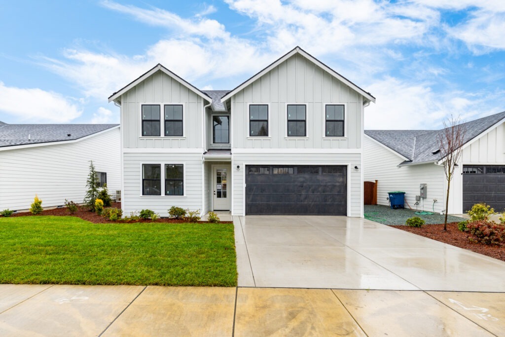 Front view of a modern white two-story house with garage and landscaped yard under a blue sky