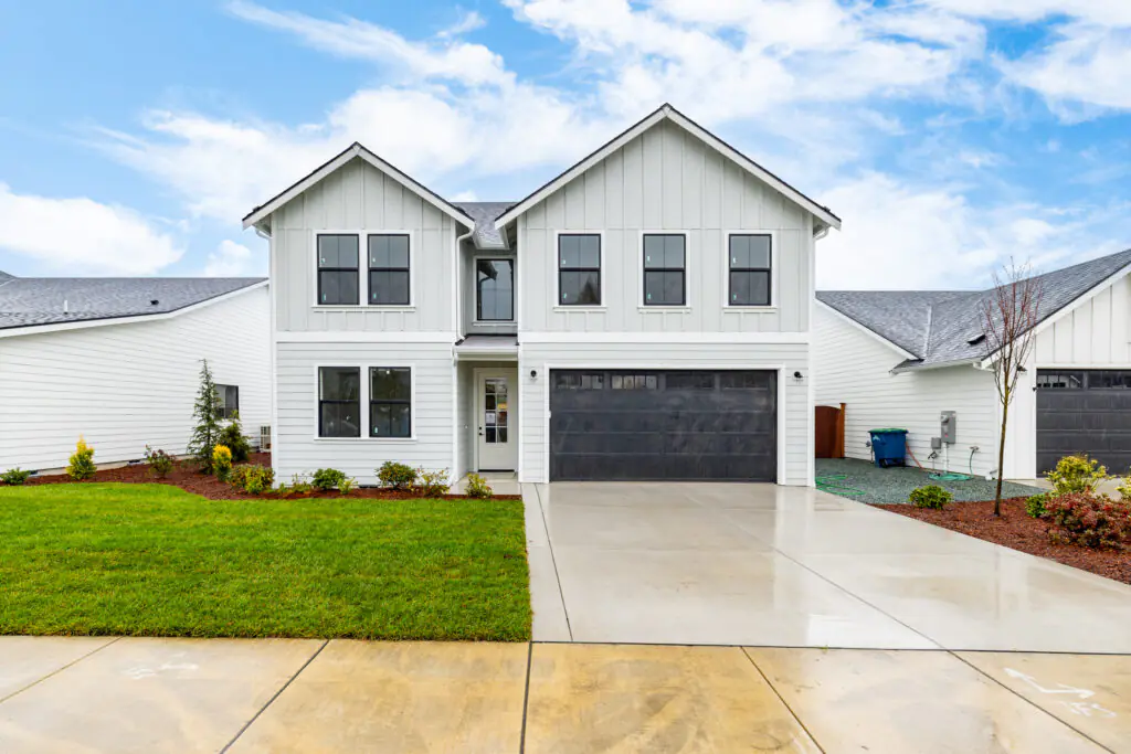 Front view of a modern white two-story house with garage and landscaped yard under a blue sky